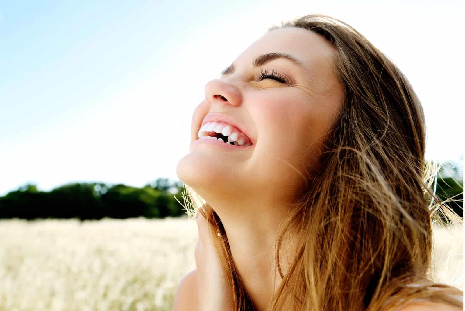 A young woman with a great smile laughs as she enjoys the sunshine out in a field.