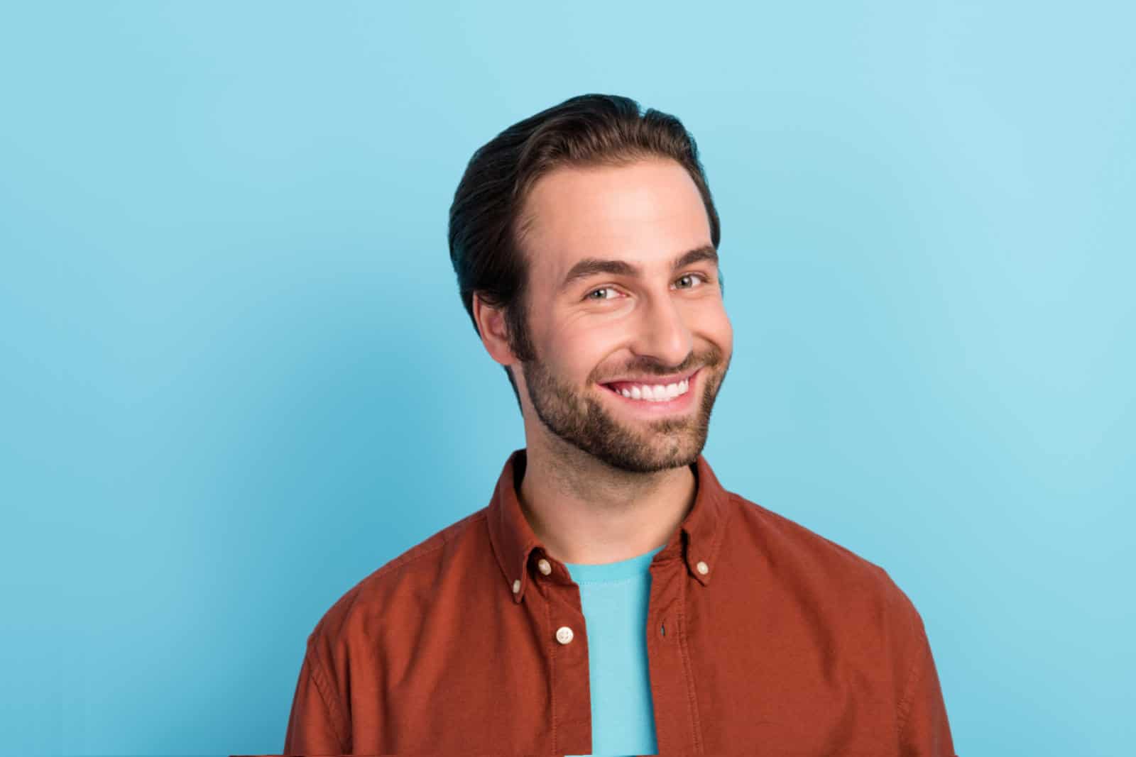 A handsome man smiles at the camera in front of a light blue background.