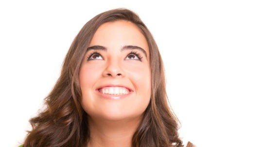 A woman with perfect teeth smiles and looks up in front of a white background.