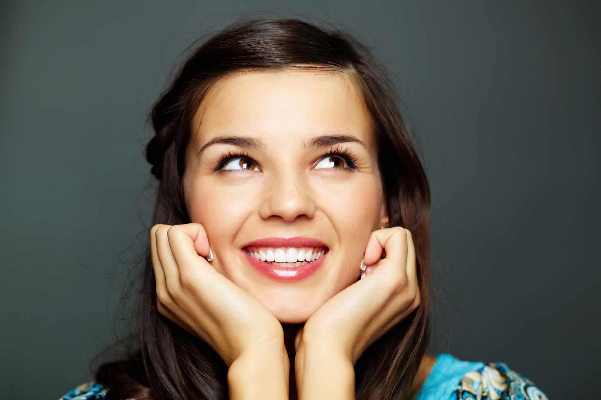 A young woman with perfect teeth smiles off screen in front of a dark gray background.